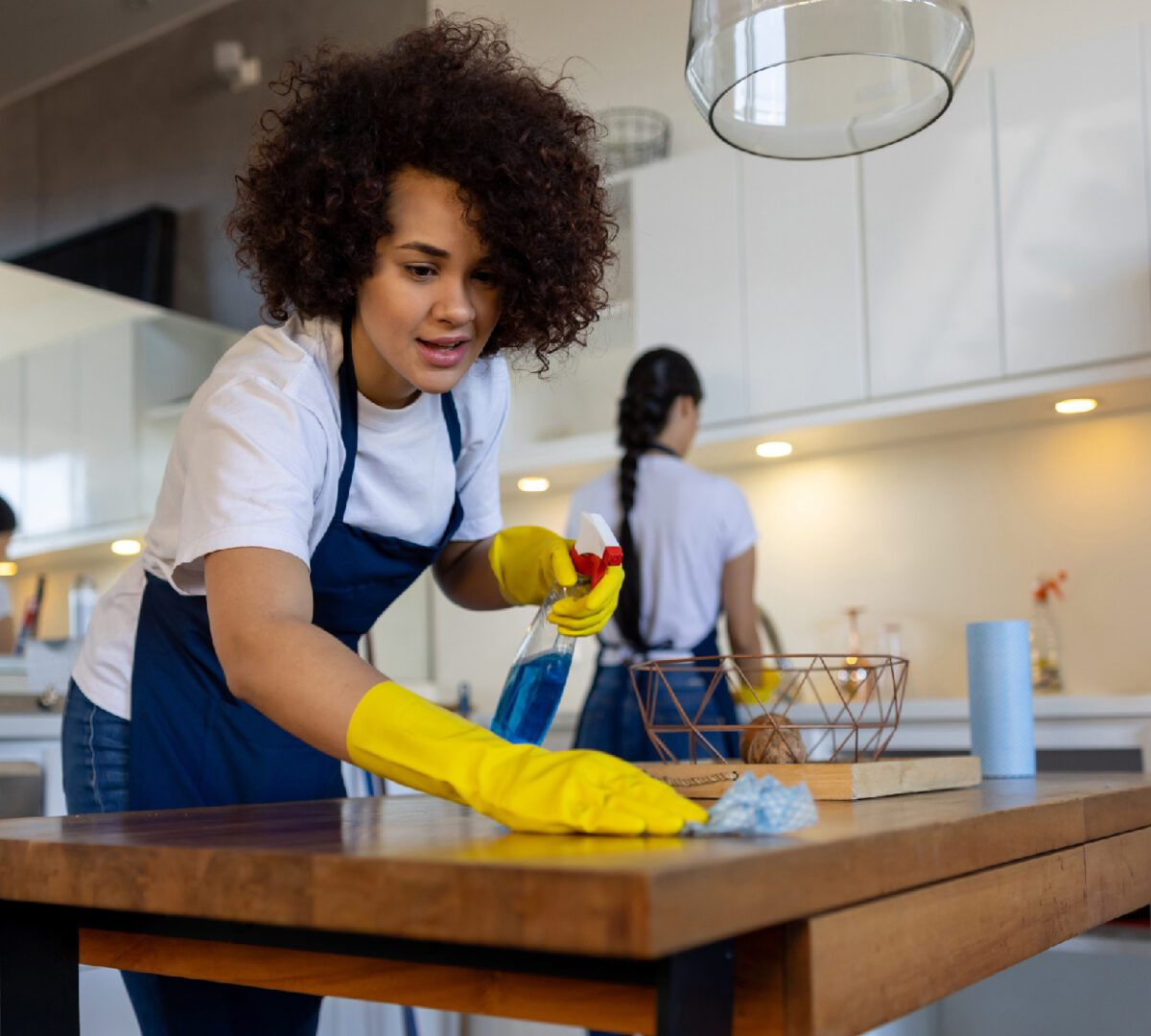 Woman cleaning a table with a cloth and yellow gloves in a kitchen.